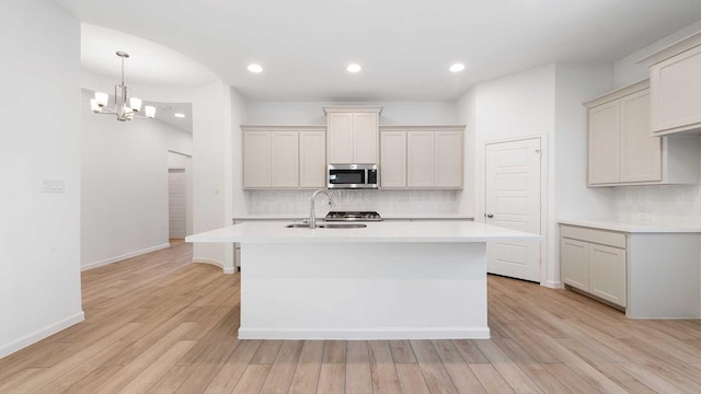 kitchen featuring sink, light hardwood / wood-style flooring, a notable chandelier, decorative backsplash, and a center island with sink