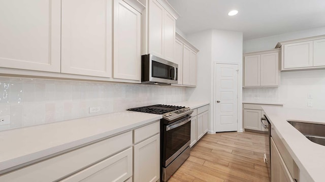 kitchen with tasteful backsplash, white cabinetry, stainless steel appliances, and light wood-type flooring