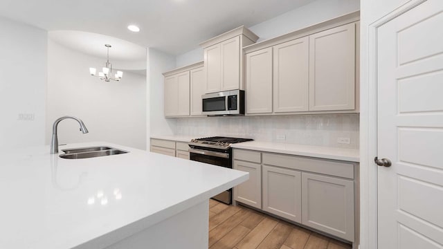 kitchen with tasteful backsplash, stainless steel appliances, sink, decorative light fixtures, and an inviting chandelier