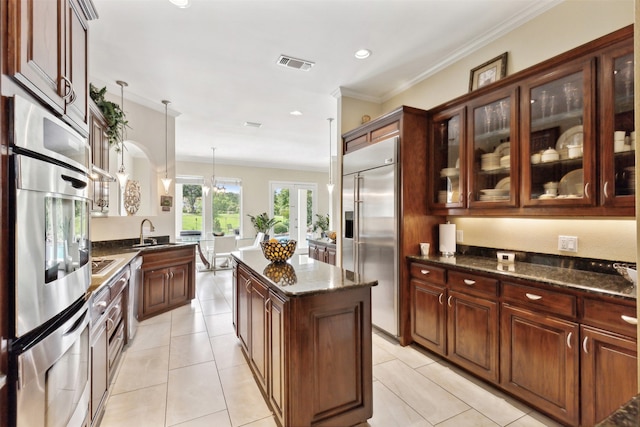 kitchen featuring appliances with stainless steel finishes, sink, pendant lighting, dark stone countertops, and a center island