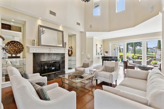 living room with wood-type flooring, a tiled fireplace, crown molding, and a towering ceiling