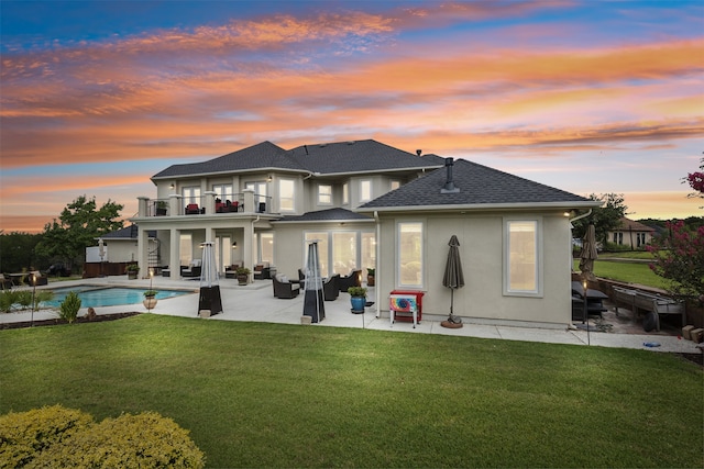 back house at dusk with a balcony, a lawn, and a patio area