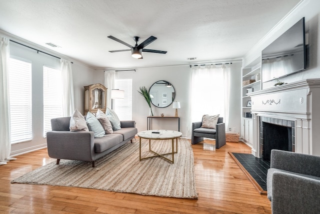 living room featuring ornamental molding, built in shelves, ceiling fan, and light wood-type flooring