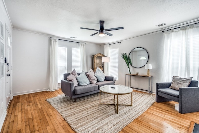 living room featuring light wood-type flooring, ceiling fan, ornamental molding, and a textured ceiling