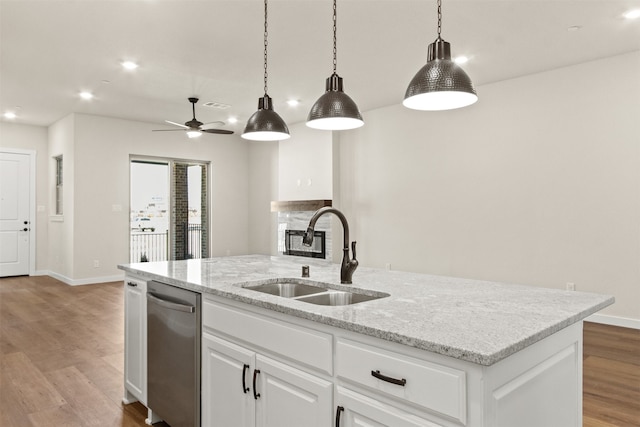 kitchen with sink, hanging light fixtures, an island with sink, light stone countertops, and white cabinets