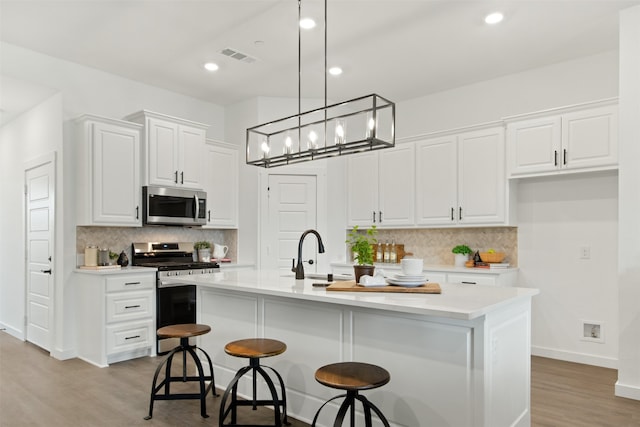 kitchen with stove, a center island with sink, light hardwood / wood-style flooring, and decorative light fixtures