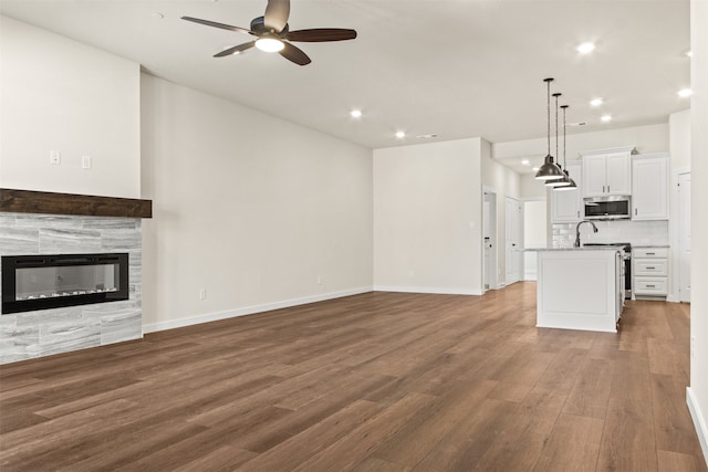 unfurnished living room with ceiling fan, dark hardwood / wood-style flooring, and a tile fireplace