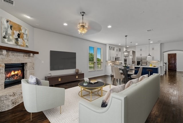 living room featuring a stone fireplace, dark wood-type flooring, and ceiling fan