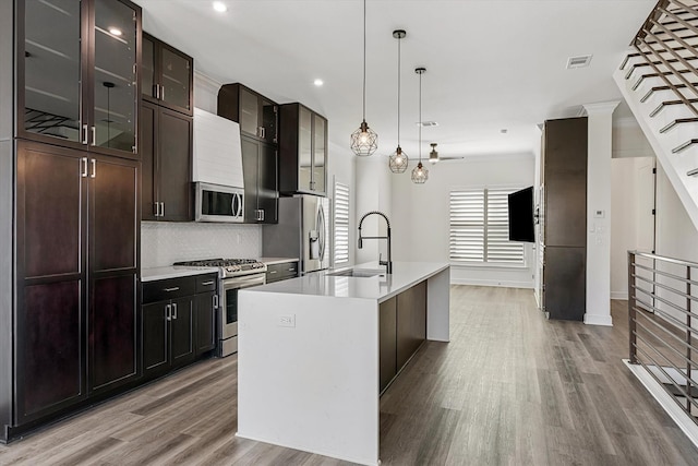 kitchen featuring stainless steel appliances, light wood-type flooring, sink, backsplash, and a kitchen island with sink