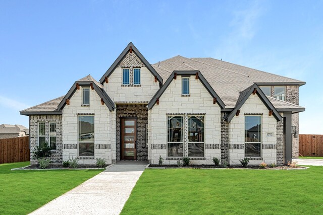craftsman house with fence, a front yard, stone siding, brick siding, and a shingled roof