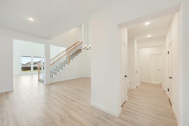 hallway with baseboards, light wood finished floors, stairs, and an inviting chandelier