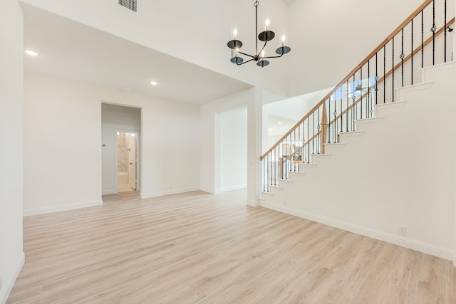 unfurnished living room featuring an inviting chandelier, a towering ceiling, and light wood-type flooring