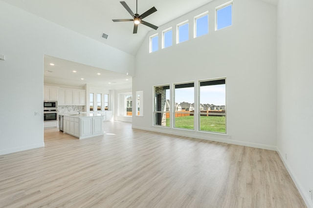 unfurnished living room with ceiling fan, visible vents, a sink, high vaulted ceiling, and light wood finished floors