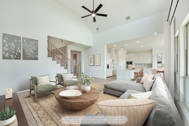 living area with a ceiling fan, visible vents, stairway, high vaulted ceiling, and light wood finished floors