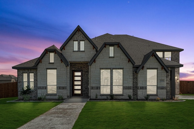 view of front facade with stone siding, fence, a shingled roof, and a front yard