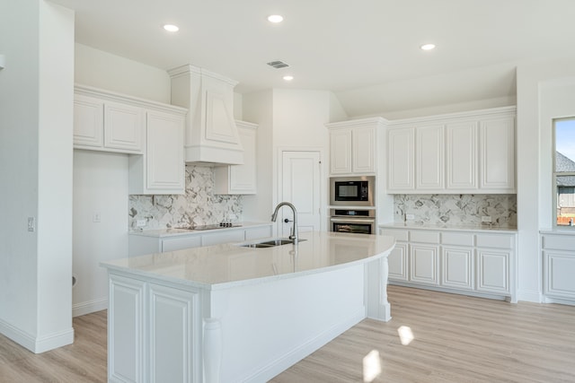 kitchen featuring a center island with sink, black appliances, white cabinets, and backsplash