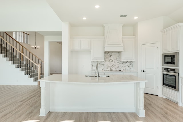 kitchen with black appliances, a kitchen island with sink, and light wood-type flooring