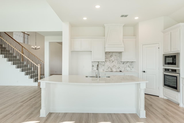 kitchen featuring a sink, light wood-style flooring, visible vents, custom exhaust hood, and black appliances