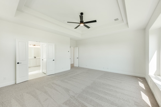 unfurnished bedroom with ensuite bath, a tray ceiling, light colored carpet, and ceiling fan