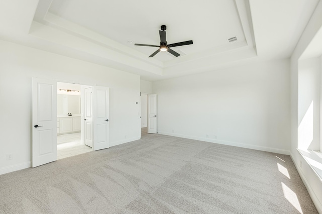 unfurnished bedroom featuring light colored carpet, a raised ceiling, ensuite bath, baseboards, and visible vents