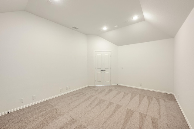spare room with light colored carpet, vaulted ceiling, and visible vents