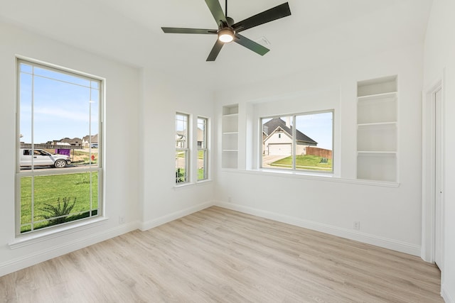 empty room featuring a ceiling fan, baseboards, built in shelves, and wood finished floors