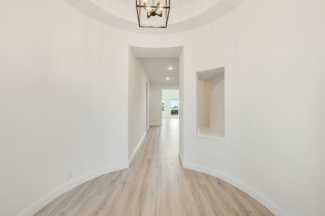 corridor featuring baseboards, light wood-style flooring, and a chandelier