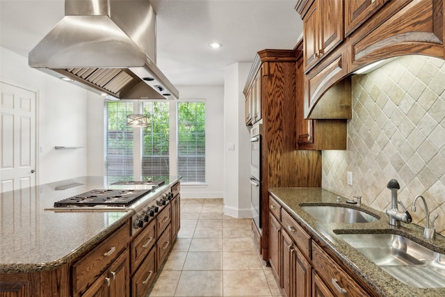 kitchen with appliances with stainless steel finishes, sink, dark stone counters, island exhaust hood, and light tile patterned floors