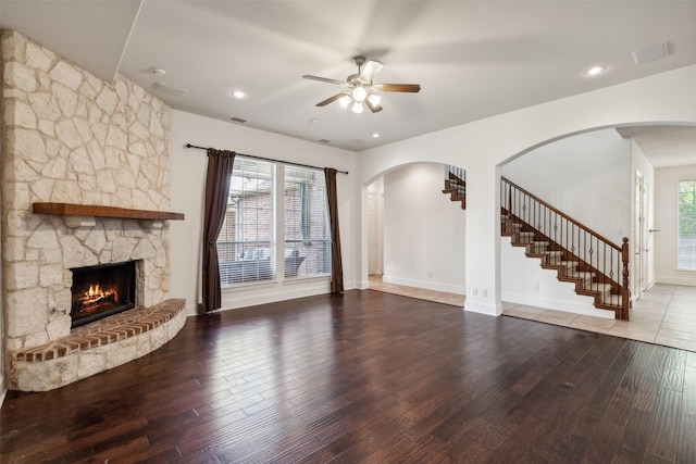 unfurnished living room with wood-type flooring, a stone fireplace, and ceiling fan