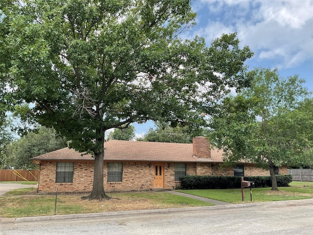 ranch-style home featuring brick siding, a chimney, a front yard, and fence