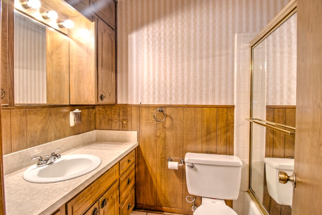 full bathroom with wooden walls, combined bath / shower with glass door, toilet, and vanity