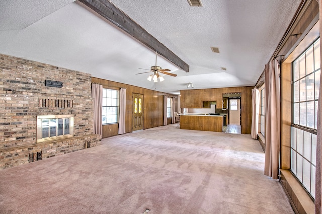 unfurnished living room featuring carpet floors, ceiling fan, wooden walls, and beam ceiling