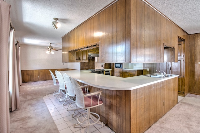 kitchen featuring ornamental molding, light carpet, kitchen peninsula, and wooden walls