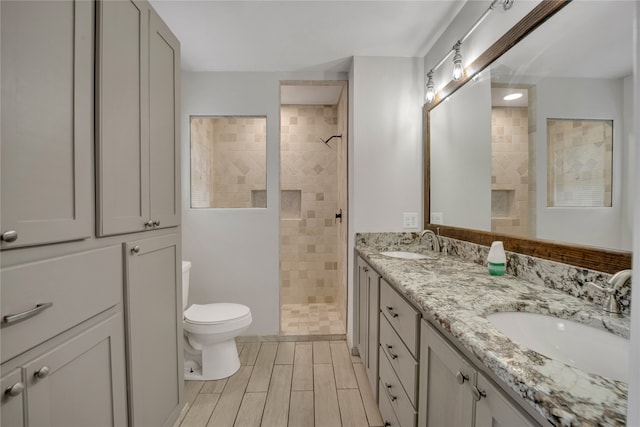 bathroom featuring double vanity, toilet, and a tile shower