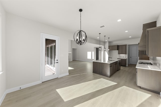 kitchen with an inviting chandelier, sink, hanging light fixtures, stainless steel gas cooktop, and a center island with sink