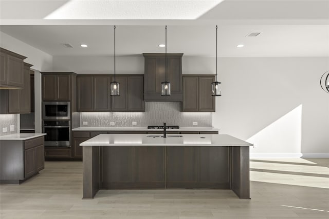 kitchen with appliances with stainless steel finishes, tasteful backsplash, a kitchen island with sink, dark brown cabinets, and hanging light fixtures