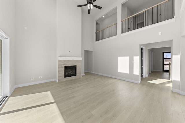 unfurnished living room with a tiled fireplace, light hardwood / wood-style floors, ceiling fan, and a towering ceiling