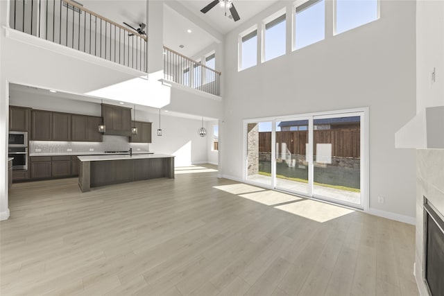 unfurnished living room with light wood-type flooring, a tiled fireplace, a wealth of natural light, and a high ceiling