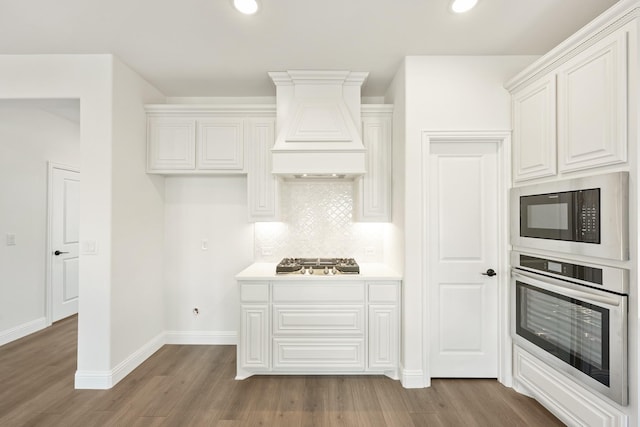 kitchen featuring appliances with stainless steel finishes, white cabinetry, tasteful backsplash, wood-type flooring, and custom exhaust hood