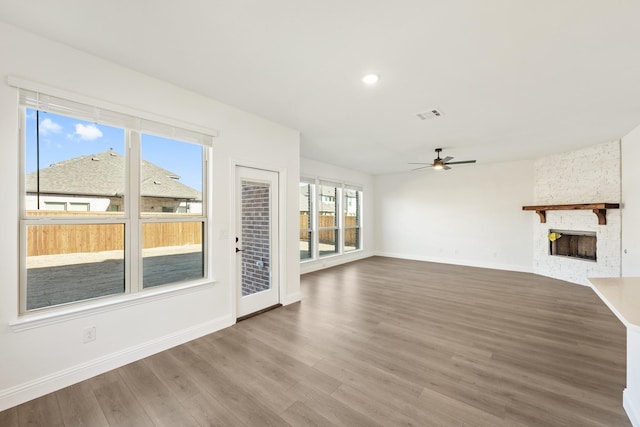 unfurnished living room with hardwood / wood-style floors, a stone fireplace, and ceiling fan