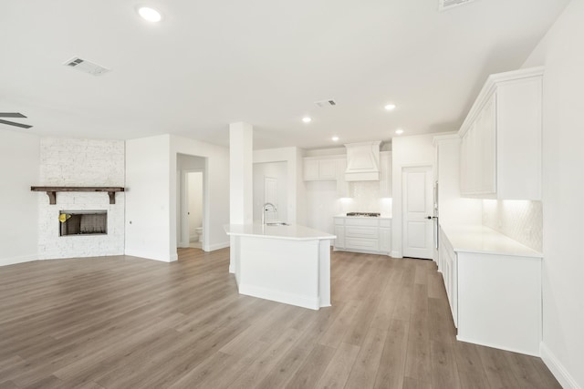 kitchen with white cabinetry, light wood-type flooring, custom exhaust hood, and a center island with sink