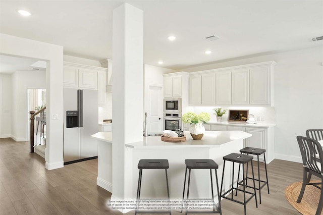 kitchen with hardwood / wood-style flooring, a breakfast bar area, appliances with stainless steel finishes, an island with sink, and white cabinets