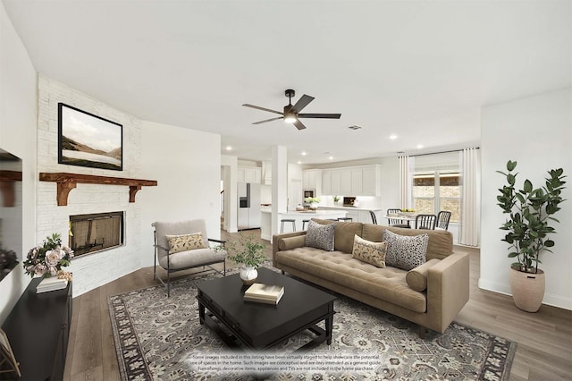 living room featuring hardwood / wood-style flooring, ceiling fan, and a stone fireplace