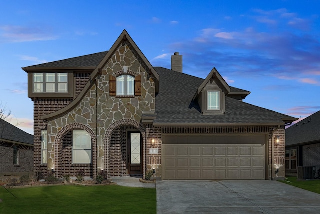 tudor house featuring a garage, central AC unit, and a lawn