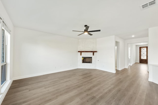 unfurnished living room featuring a stone fireplace, light hardwood / wood-style floors, and ceiling fan