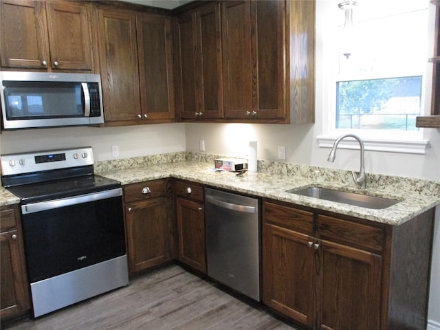 kitchen featuring light stone countertops, appliances with stainless steel finishes, sink, and light hardwood / wood-style floors