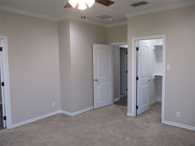 unfurnished bedroom with crown molding, a spacious closet, light colored carpet, and ceiling fan