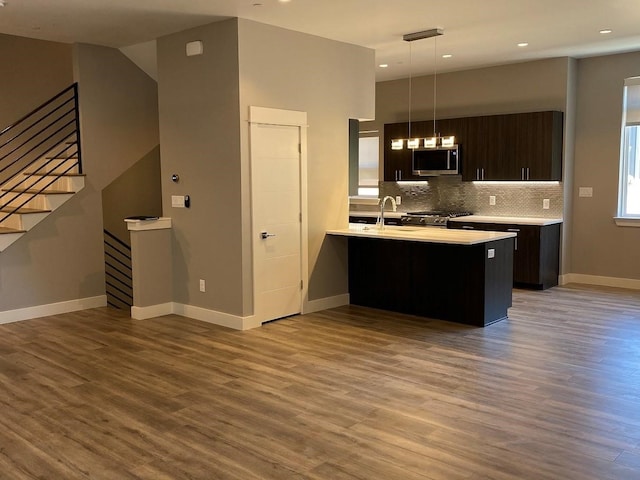 kitchen with kitchen peninsula, backsplash, hardwood / wood-style flooring, dark brown cabinetry, and stove