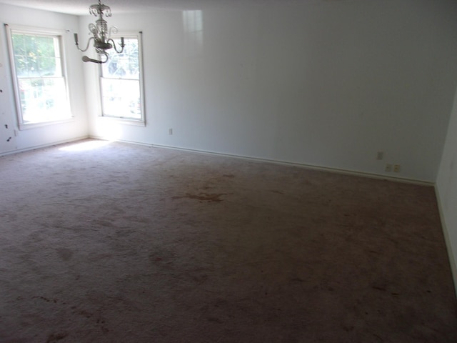 carpeted empty room with a notable chandelier