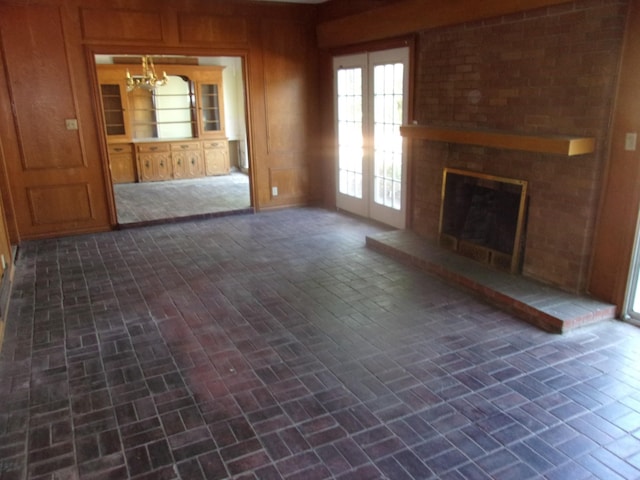 unfurnished living room featuring french doors, a brick fireplace, and a notable chandelier